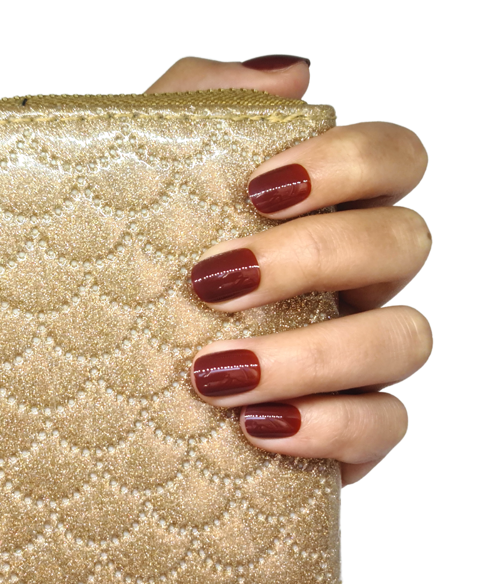 Faux ongles marron chaud posés sur main fermée, courts arrondis, brillance visible