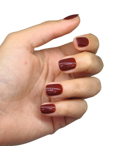 Faux ongles marron chaud posés sur main fermée, courts arrondis, brillance visible